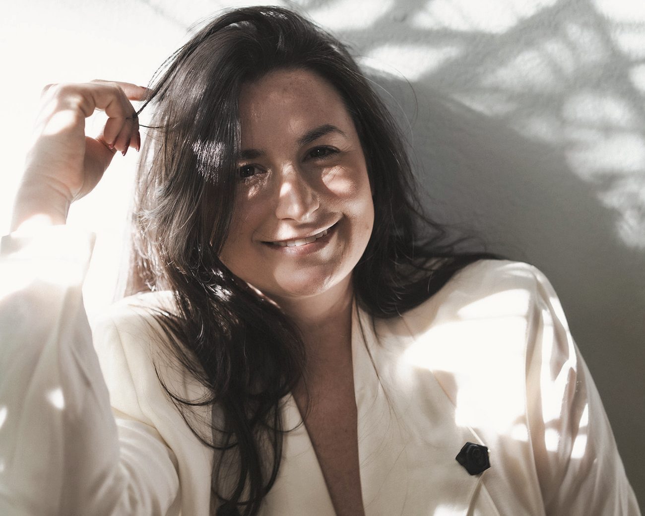 Jade Levinson smiling in a cream blazer, sunlight and leaf shadows across her face