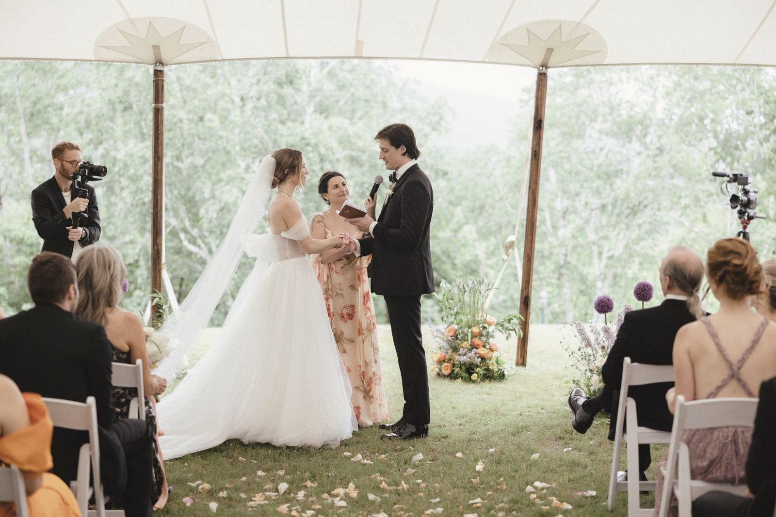 Jade officiating a wedding under a sailcloth tent as the groom reads his vows