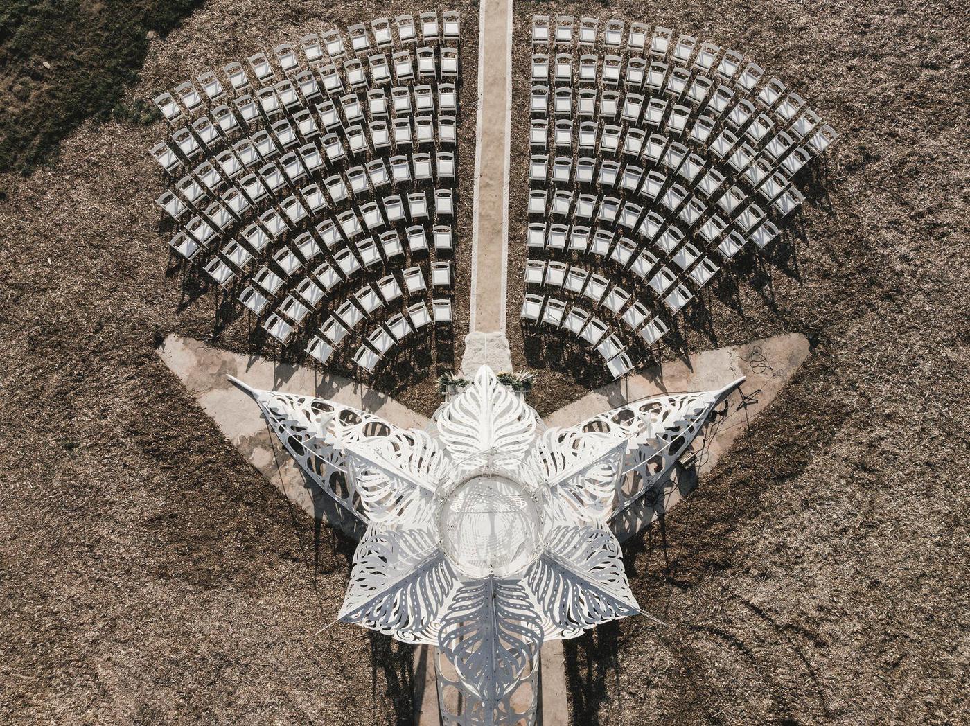 Aerial view of a spiraling white altar and curved rows of chairs in a field